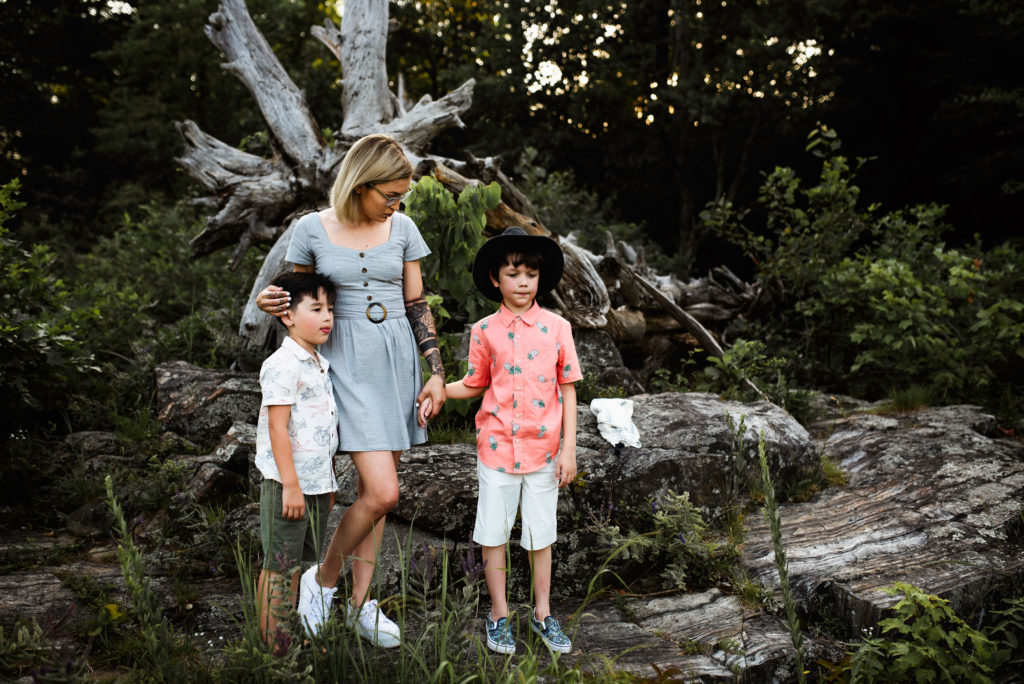A family wears white, blue, and coral agains the dark green trees for their family photos. The pop of color stands out against the dark background.