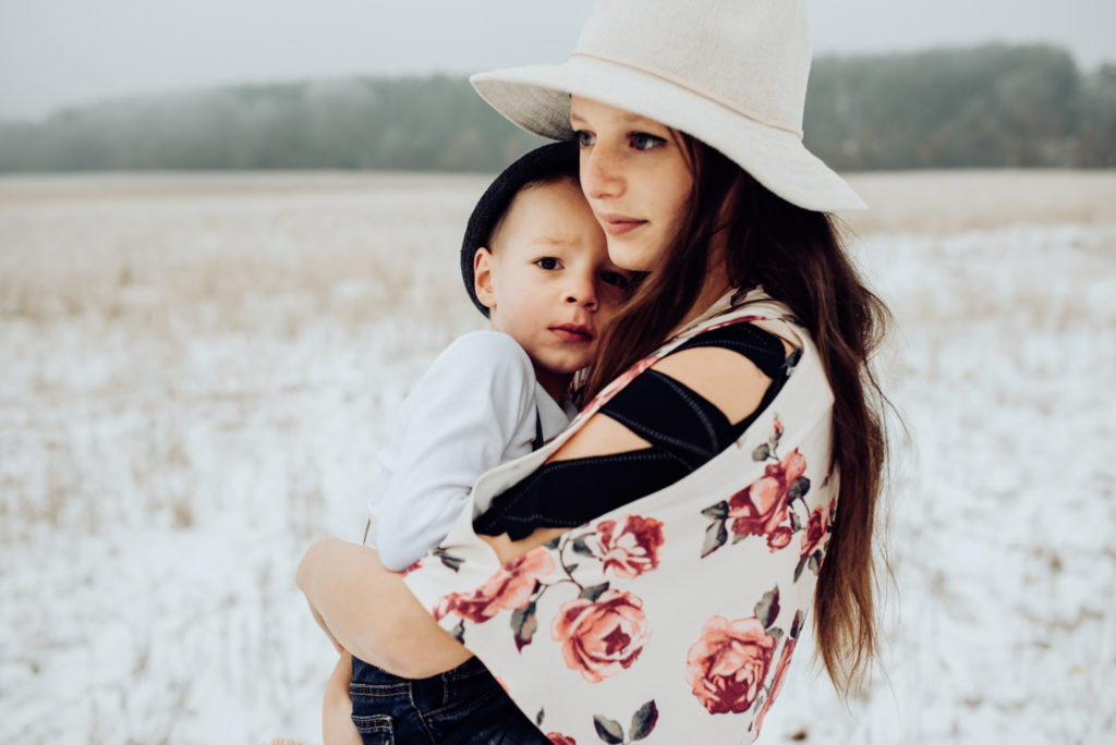 An older sister carries her baby brother through a snowy field during family photos.